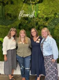 image from left to right - Audrey, Regan, Jessica and Amanda standing in front of a green moss wall with the word 